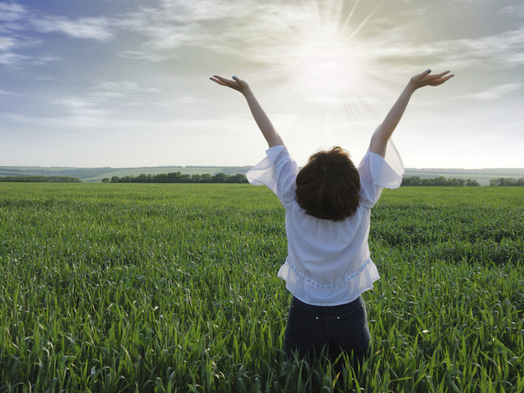The girl on a field. The woman with the lifted hands to the sky on a green meadow