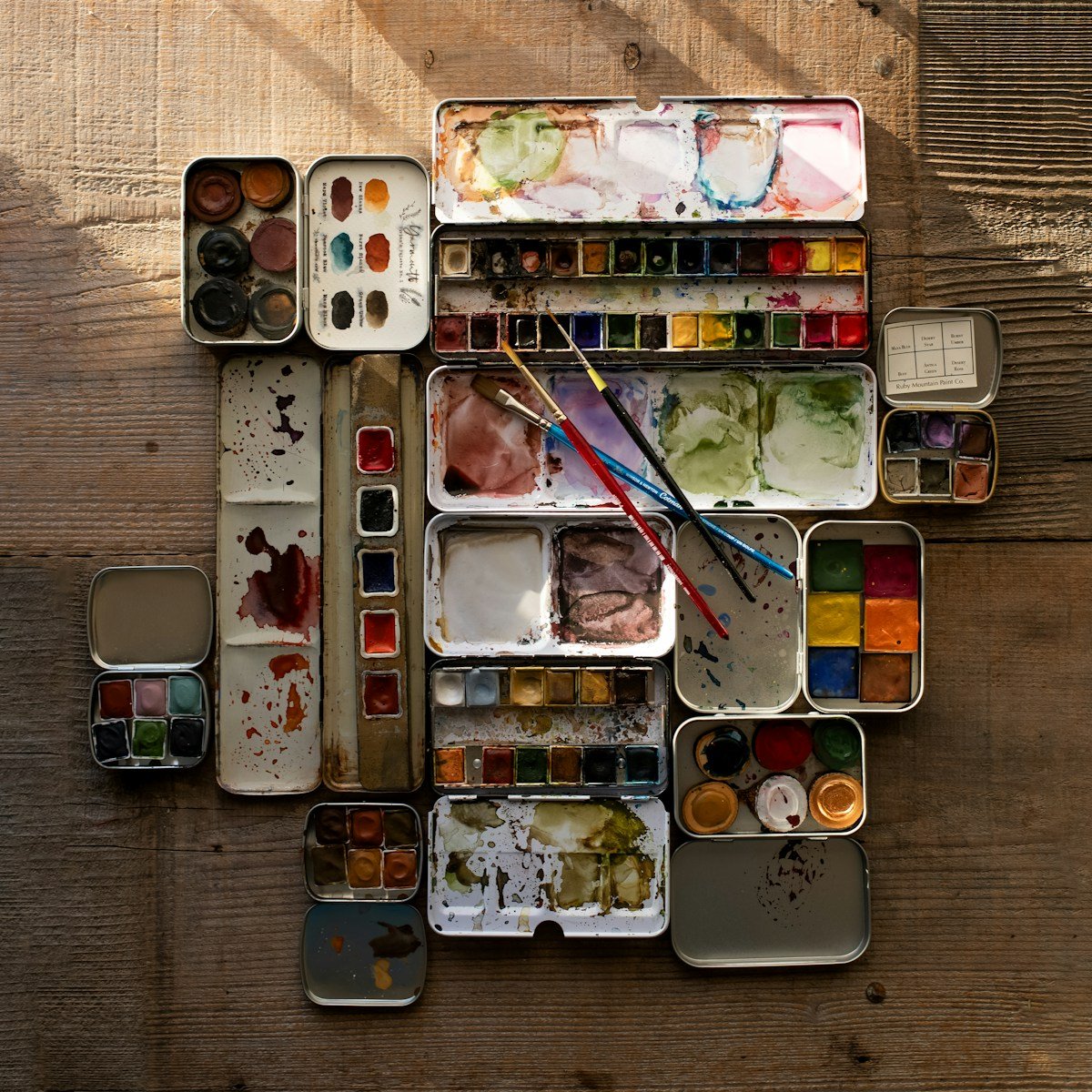 a wooden table topped with lots of paint and brushes